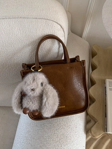 Sac seau marron vintage avec pendentif lapin en peluche sur fond de canapé bouclé