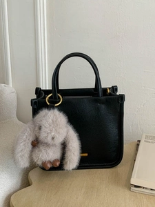 Sac à main rétro en cuir noir avec pendentif lapin en peluche sur un canapé blanc