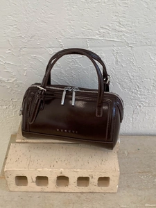 Modern dark brown glossy Boston handbag with top handles and textured wall background