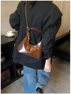 Détail d'un sac demi-lune marron avec gland en perles de bois et logo doré imprimé dessus