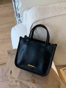 Sac seau minimaliste en cuir noir avec logo doré sur fond de trench-coat élégant et moderne