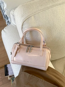Pink faux leather mini Boston bag with dual handles and silver hardware on a soft couch