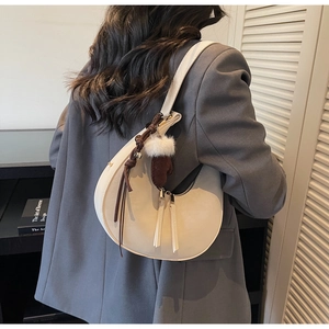 Dettaglio della borsa a mezzaluna beige indossata a spalla con ciondolo in corda intrecciata