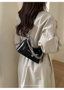 Detail of black glossy trapezoid shoulder bag with silver chain and heart pendant