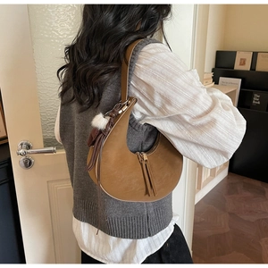 Vista posteriore di una modella con borsa a mezzaluna marrone e ciondolo a pompon bianco