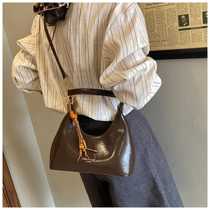 Detail of dark brown glossy underarm bag with orange beaded tassel and shoulder strap