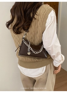 Detail of chocolate faux leather bag with silver chain and heart pendant on shoulder