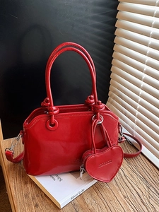Retro red handbag with knot handles, heart charm and detachable strap on a desk