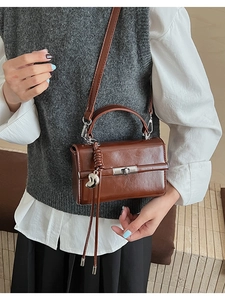 Detail of dark brown glossy leather handbag with silver twist lock and heart pendant