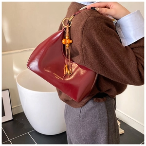 Detail of burgundy glossy underarm bag with decorative orange wood tassel and golden text