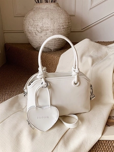 Minimalist white cylindrical handle handbag with a heart charm on a textured background