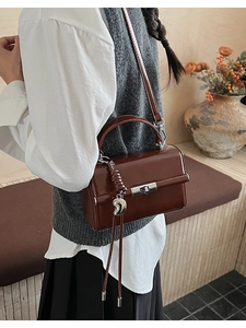 Detailed side view of brown glossy square handbag with silver moon charm and tassel