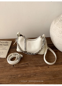 Close-up of white oil wax leather bag with silver chain on textured wood