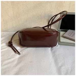 Detail of dark brown patent leather shoulder bag with decorative knotted straps and metallic tips