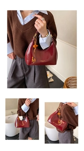 Détail du sac hobo en cuir verni bordeaux avec pompon en bois et anneau doré