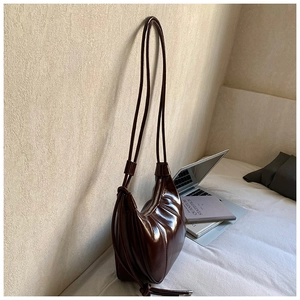 Detail of a dark brown crescent bag with pleated sides and glossy leather texture