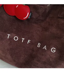 Macro detail of dark brown suede tote bag with white lettering and red cherry charm