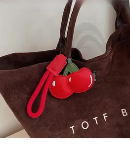 Detail of red cherry PU leather charm with green leaves on a brown textured tote bag