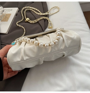 Close-up of white ruched bag featuring pearl handle and gold chain strap detailing