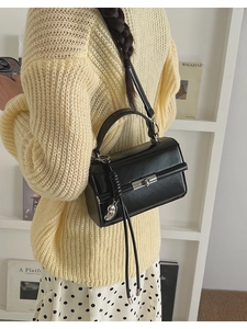 Detail of black glossy leather handbag with silver twist lock and tassel charm accessory