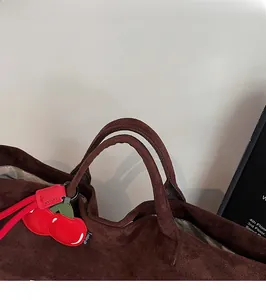 Detailed view of a dark brown suede tote bag featuring a red cherry charm and sturdy handles