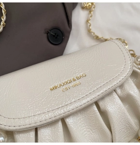 Detailed macro view of white pleated leather bag with gold chain and pearl strap