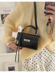 Detail of glossy black patent leather handbag with silver twist lock and woven strap