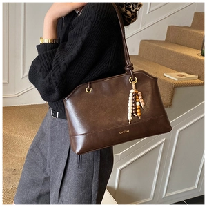 Detail view of dark brown leather tote bag with wood bead tassel and logo branding