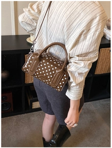Detailed side view of a brown polka dot boston bag worn by a model in casual wear