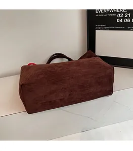 Detail view of large dark brown suede tote bag on marble surface with sturdy handles