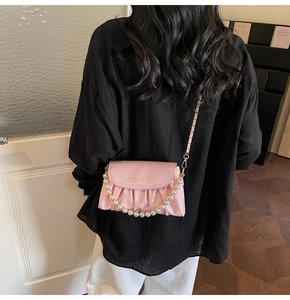 Pink pleated cloud bag with pearl handle and gold chain strap shown on a shoulder