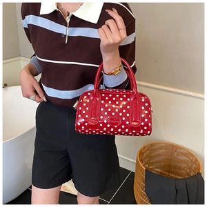Close-up of a red polka dot Boston bag featuring a branded logo plate and metal zippers