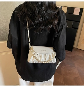 Rear view of a white ruched cloud bag with pearl strap and metal chain over a black shirt
