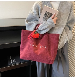 Detail of burgundy suede tote bag featuring white TOTF text and cherry charm accessory