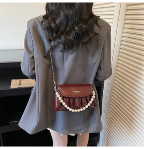 Detail of burgundy ruched leather shoulder bag with pearl handle and chain strap on model