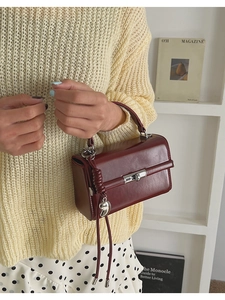 Detail of burgundy handbag with silver heart pendant, fringe and woven handle
