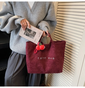 Detail of burgundy suede tote bag featuring a cherry pendant and white text print