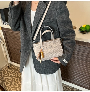 Détail du sac à main beige texturé avec breloque en perles de bois et bandoulière
