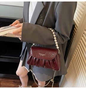 Detail of burgundy ruched bag featuring white pearl handle and golden chain strap