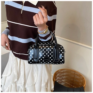 Close-up of a black and white polka dot handbag with round top handles and metal logo