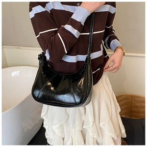 Detail of black patent leather crescent hobo bag with contrast stitching on shoulder