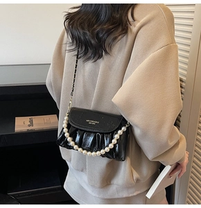Detail view of black pleated cloud bag with faux pearl chain and gold brand logo