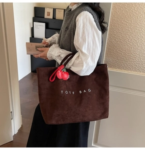 Detail of brown suede tote bag with white embroidery and red cherry pendant charm