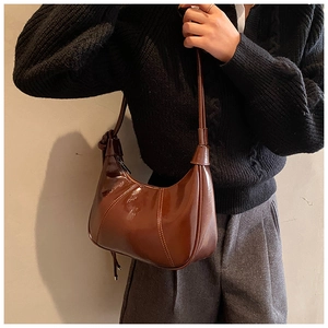 Detailed side view of brown glossy hobo bag with contrast stitching and knot detail