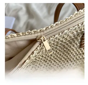 Détail de la fermeture éclair dorée et de l'anse en cuir sur le sac cabas en paille