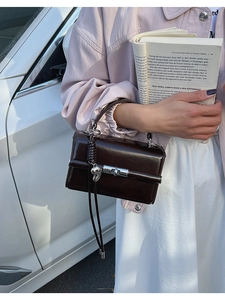 Detail showing glossy chocolate leather texture and metallic heart charm on a square bag