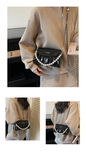 Close-up of black ruched cloud bag featuring pearl handle and gold chain strap
