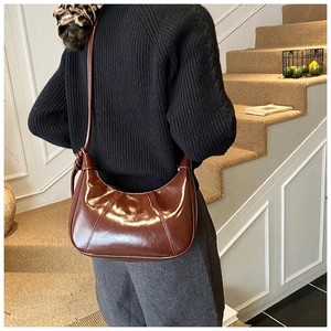 Polished reddish-brown crescent shoulder bag shown on a model in a minimalist setting