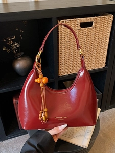 Deep red patent leather underarm bag with a half-moon shape and wooden gourd tassel