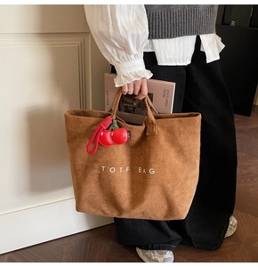 Detail of dark brown corduroy tote bag featuring TOTE BAG text and a red cherry charm